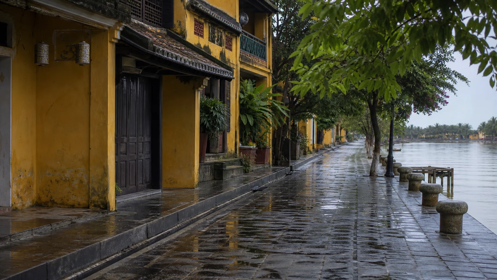 Hoi An riverside heritage buildings after rain with visible drainage and calm water