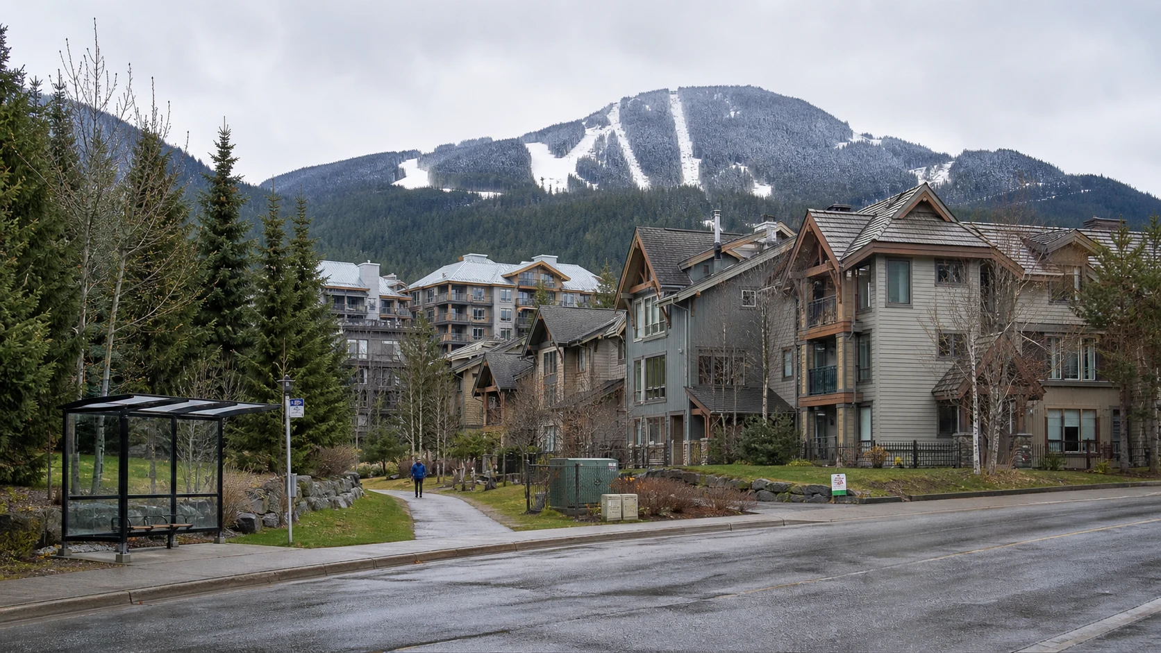 Whistler Creekside housing beside a bus stop and paved trail with the mountain behind